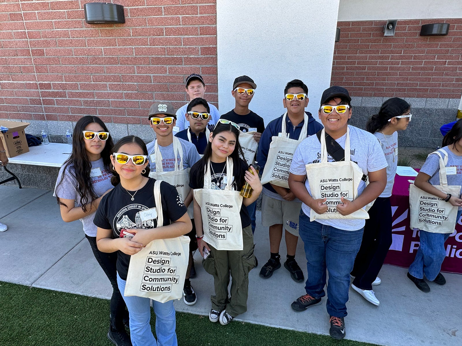 group of students smiling, wearing yellow-tinted sunglasses, and holding "Design Studio for Community Solutions" tote bags 