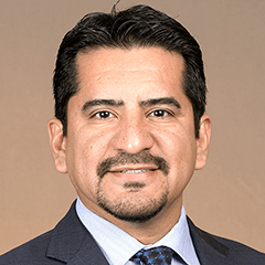 Alberto Olivas headshot - fair-skinned man, smiling, black hair and mustache, gray blazer, white collared shirt, blue tie 