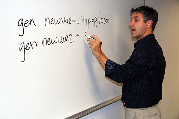 male professor with black hair and a navy collared shirt writing on a whiteboard