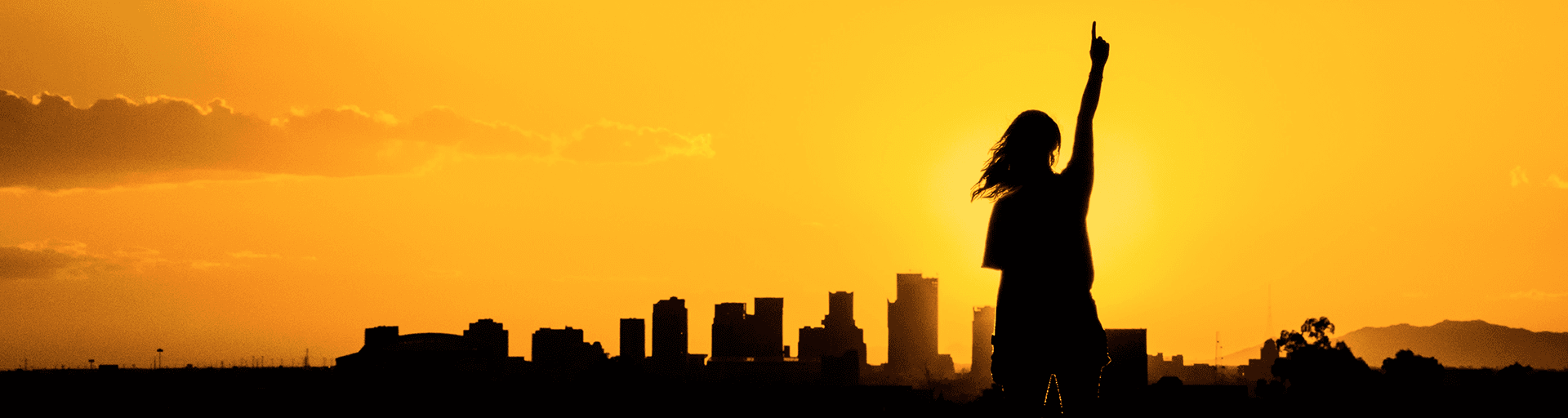 silhouette of a person pointing upward against a golden background with ASU buildings