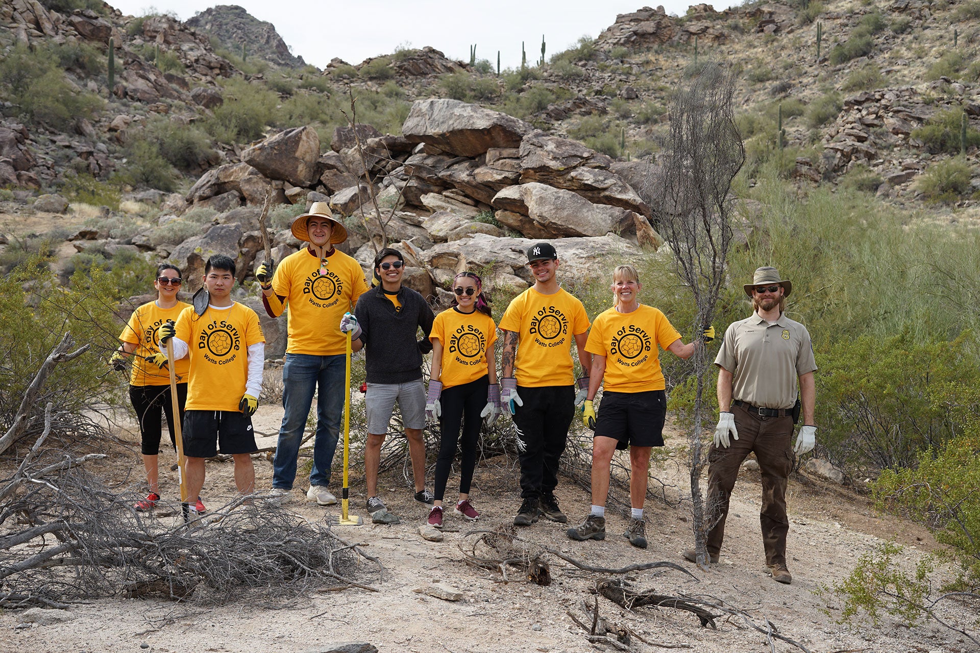 group of eight people hiking in the Arizona mountains and wearing gold Watts College Day of Service shirts