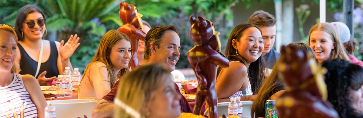 ASU alumni smiling and talking at tables with food, drinks, and Sparky the Sun Devil figurines 