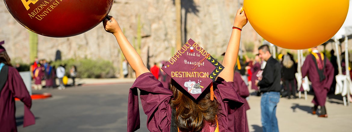 college graduate wearing a cap and gown and holding two ASU balloons in the air 