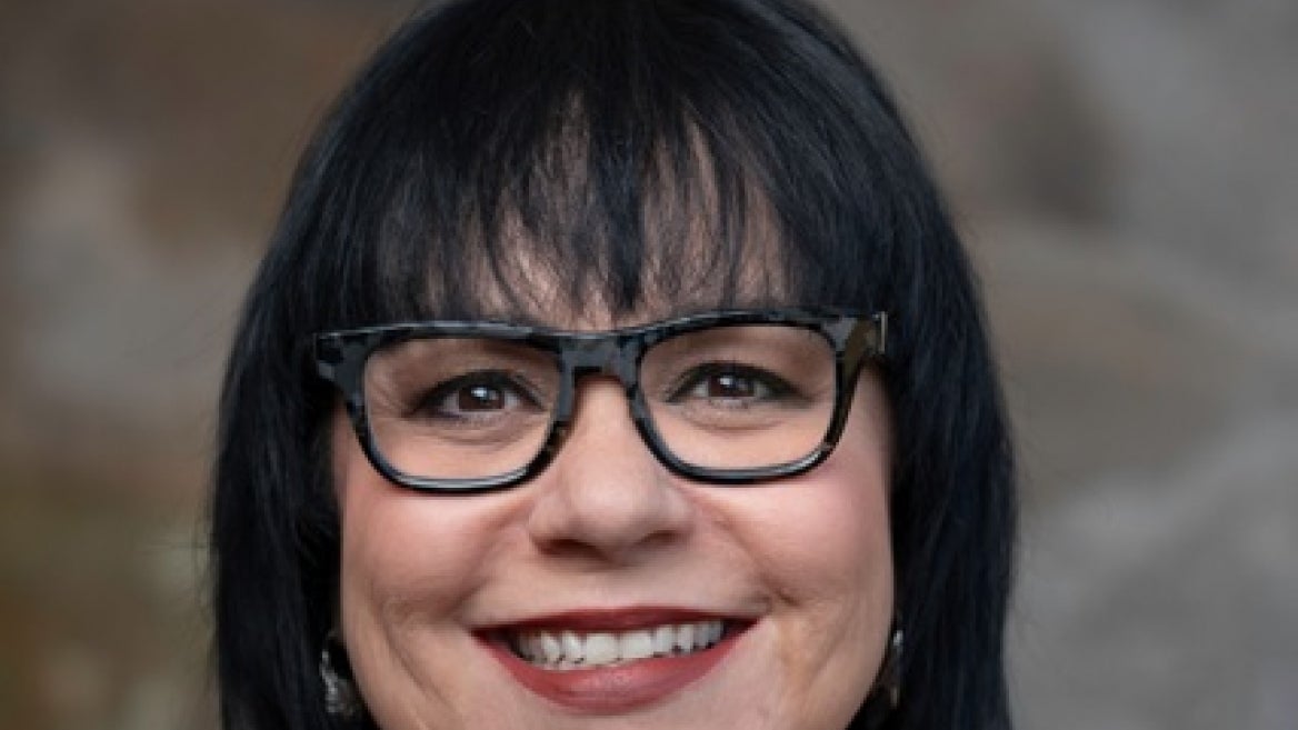 Traci Morris headshot - fair-skinned woman, smiling, black hair, glasses, gray shirt 